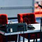 Two red empty chairs, microphone and sound mixer at press conference hall.