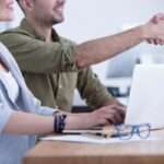 Close-up on a young businesswoman by a laptop and her blurry colleague sitting beside shaking hands with a candidate after a job interview